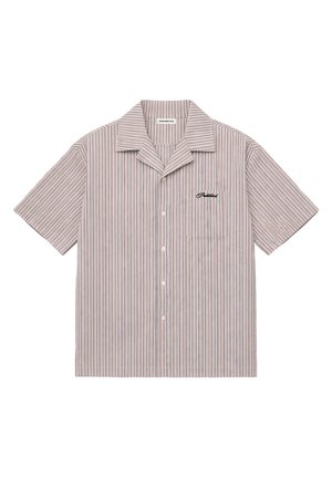 Femme portant une casquette blanche, une chemise à boutons rayée verticalement à manches courtes par-dessus un haut blanc et un short vert foncé, regardant vers le bas.