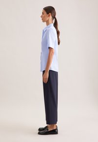 Camicia a maniche corte blu e pantaloni blu scuro. La camicia presenta un colletto a punta e una silhouette dritta. Mocassini neri completano l'outfit.