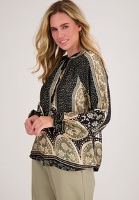 Langsleeve blouse in zwart, groen en beige met bloemen- en paisleypatronen. Heeft gathered mouwen en een striknek.