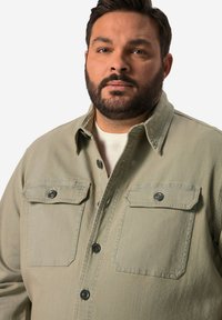 Vihreä vaaleanvihreä nappipaita, joka on valmistettu pehmeästä kankaasta. Paidassa on kaksi rintataskua ja mustat nappikoristeet. Kauluspaita, jossa on rento malli.