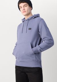 Felpa grigio-blu con tasca a marsupio frontale, cappuccio con cordino e polsini a coste. Presenta una piccola etichetta del marchio sul petto.