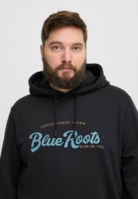Schwarzer Kapuzenpullover aus weichem Stoff, mit dem „Blue Roots“-Logo in hellblauem und braunem Text, mit Kordeln und lockerer Passform.