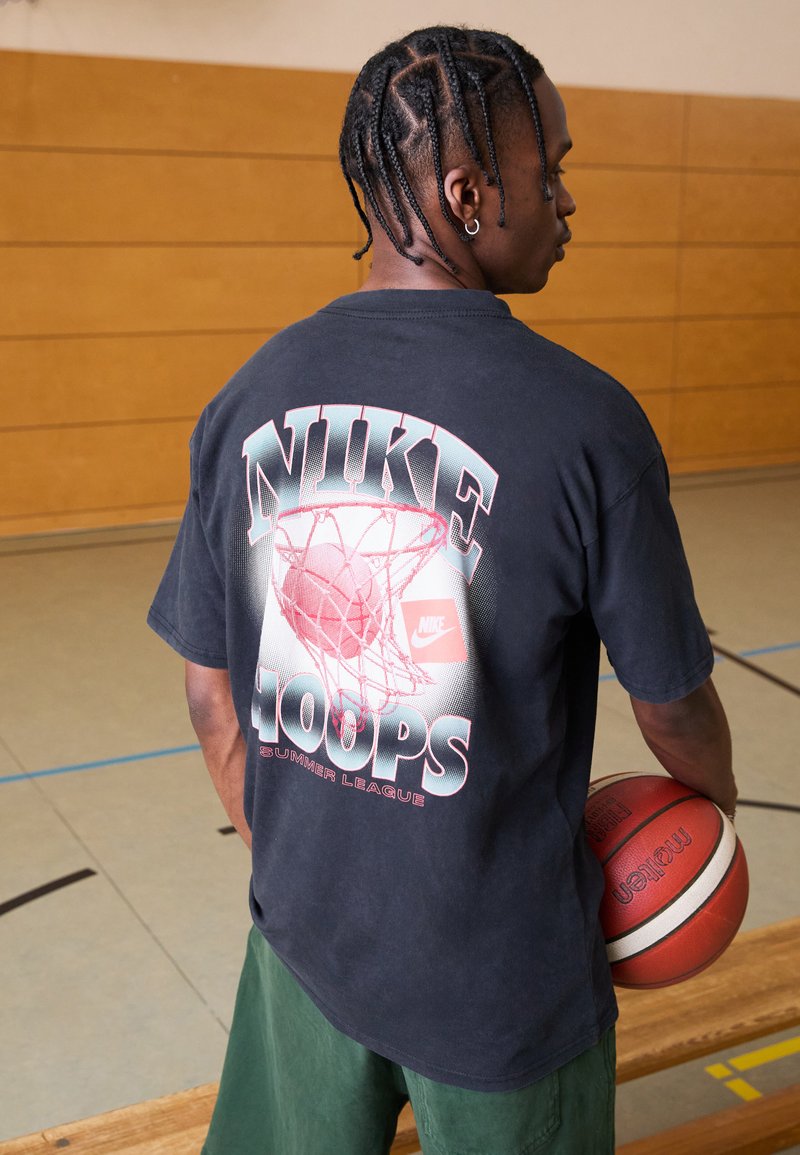 Camiseta negra de Nike con un gran gráfico de una red de baloncesto y el texto "HOOPS SUMMER LEAGUE" en blanco y rosa. Manga corta, corte relajado.