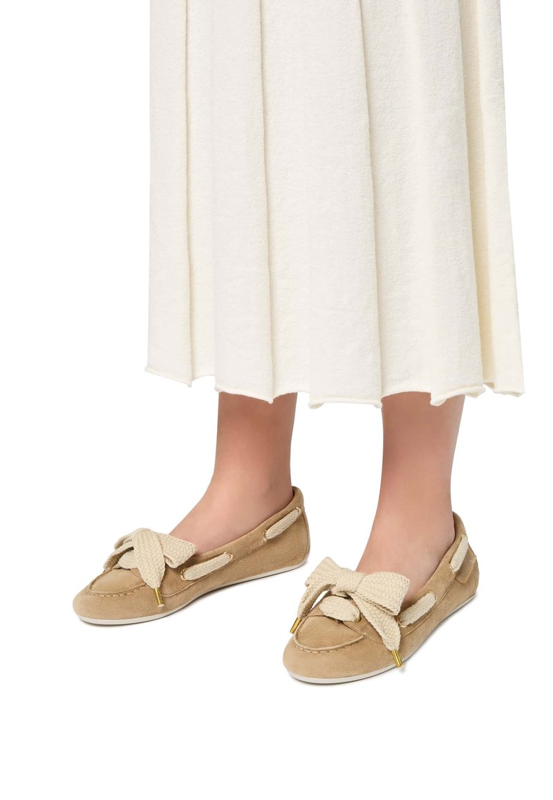 Scarpe slip-on in suede beige con un grande fiocco in corda beige, dettagli in metallo dorato e una suola in gomma bianca acontrastante.