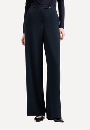 Pantaloni a gamba larga in navale con un tessuto testurizzato, dotati di chiusura con bottone e tasche frontali. Abbinati a un top aderente e ballerine nere.