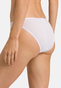 Slip in cotone bianco con un design a vita bassa, caratterizzato da una texture liscia e da una minima rifinitura di cuciture in vita e alle aperture delle gambe.