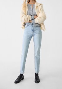 Ljusblå högmidjade jeans, grå knapprad cardigan och krämfärgad oversized stickad tröja. Svarta loafers med texturerade detaljer.