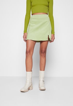 Jasnozielona mini spódnica z sztruksu z bocznym rozcięciem; zestawiona z kremowymi botkami do kostki i zielonym topem z długim rękawem i krótkim krojem.