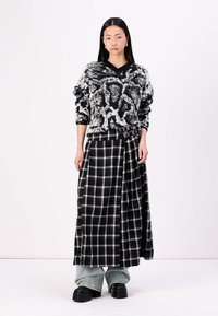 Maglione a righe bianche e nere con maniche lunghe, abbinato a una lunga gonna a quadri in bianco e nero con dettagli a fibbia. Scarponi neri con plateau.