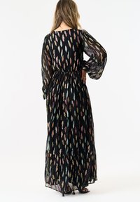 Black, long-sleeve maxi dress with a fitted waist and flowy silhouette. Features colorful feather patterns and sheer fabric with a textured finish.