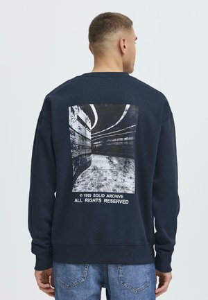 Navy sweatshirt with a back graphic featuring a black-and-white architectural image, ribbed cuff and waistband, relaxed fit.