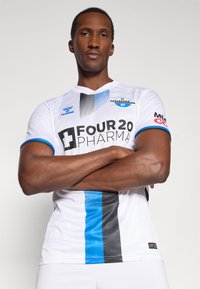 Maglia da calcio bianca con strisce nere e blu, con logo "FOUR 20 PHARMA", logo Hummel, collo rotondo e maniche corte.