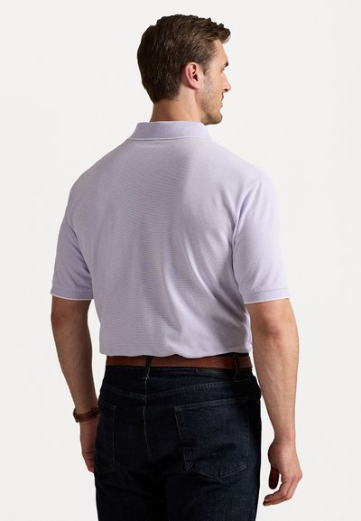 Λιλά πόλο μπλουζάκι με υφή, κοντομάνικο, και με γιακά, φορεμένο με σκούρο τζιν παντελόνι και καφέ δερμάτινη ζώνη.