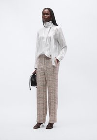 Shiny white blouse with a neck tie, paired with patterned wide-leg trousers in beige and pink tones, and black heeled sandals.