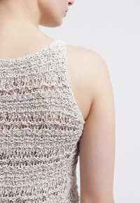 Top in maglia grigio chiaro con un motivo a intreccio aperto, dotato di spalline sottili e design con scollatura a marinara, che mette in risalto il tessuto testurizzato.