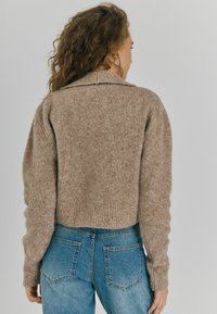 Suéter de punto beige con cuello redondo y dobladillo acanalado, combinado con jeans de mezclilla azul que tienen dos bolsillos traseros. Material texturizado y acogedor.