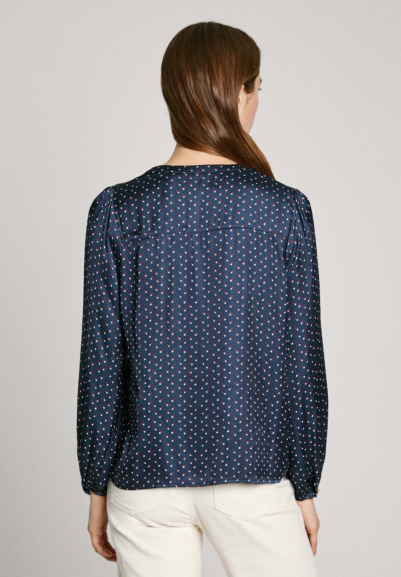 Blusa azul marino con lunares blancos y rojos, de mangas largas con puños elásticos y escote redondo. Textura suave y corte holgado.