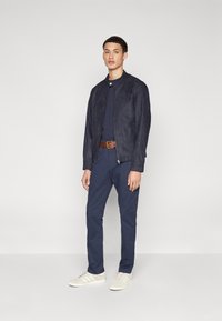 Tumes suede bomber-jakk, sobiv tumes t-särk, tumes püksid, pruun vöö ja beežid tennisetossud valgete detailidega. Sile tekstuur, stiilne disain.