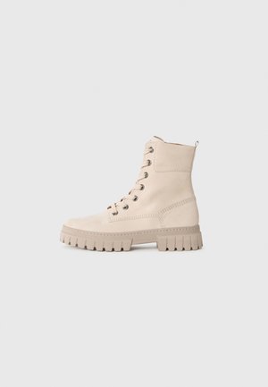 Bottes chelsea en suède beige avec un bout rond, à lacets, œillets en argent et semelle en caoutchouc robuste dotée de motifs de crampons prononcés.