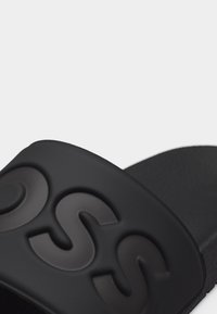 Μαύρο σανδάλι slide με ανάγλυφο λογότυπο "SS" στην φαρδιά λουρίδα πάνω από το πόδι.