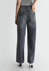 Wijde donkergrijze jeans met een hoge taille, uitgerust met twee achterzakken en een klein ritszakje, in combinatie met witte hoge hakken.