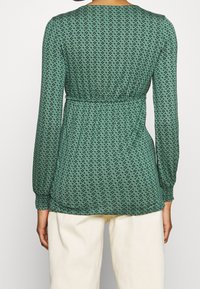 Zelen�ý dlouhý rukáv top s diamantovým vzorem, nařaseným pasem, hladkým materiálem a kulatým výstřihem, nošený přes krémové kalhoty.