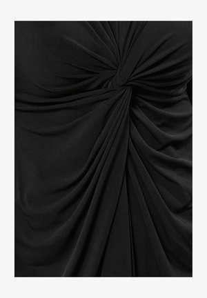 Zwarte jersey top met een gedraaide knoopdetail in het midden, met vloeiende, gedrapeerde stof die zachte texturen en vloeiende lijnen creëert.