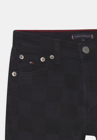 Černé džíny z denimu s kostkovaným vzorem, stříbrnými doplňky a štítkem Tommy Hilfiger na pasu s červenými stehy.