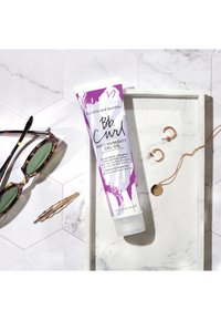 Bumble and bumble Bb. Curl Anti-Humidity Gel-Oil i en tub med en lila och vit design. Inkluderar solglasögon, en hårklämma, örhängen och ett halsband.