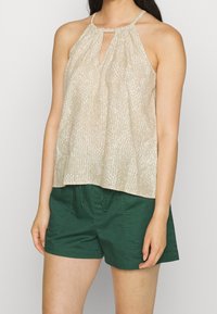 Haut halter beige clair avec un motif texturé et un détail en trou de serrure, associé à un short vert avec cordon de serrage et poches avant.