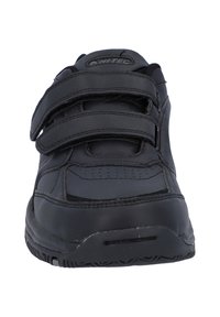 Zwarte sportieve schoen met drie klittenbandsluitingen, een bovenwerk van glad leer, een geperforeerd ontwerp op de tenen en een gestructureerde rubberen zool.