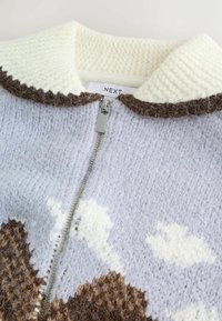Knit zip-up sweater in light blue with cream collar, brown accents, and cloud patterns. Features a textured finish and silver zipper.