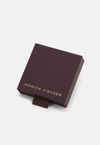 Tumši brūns rotaslietu kaste ar teksturētu virsmu, kas satur zelta logo ar uzrakstu "MONICA VINADER" un brūnu cilpu.