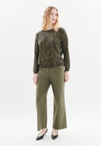Maglione a stampa leopardata in verde e marrone, abbinato a pantaloni larghi color oliva. Tacchi a punta neri completano l'outfit.