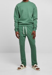 Sweat-shirt en coton vert et pantalon assorti avec cordon blanc, dotés de poignets côtelés et d'une coupe décontractée. Portés avec des sandales de couleur claire.