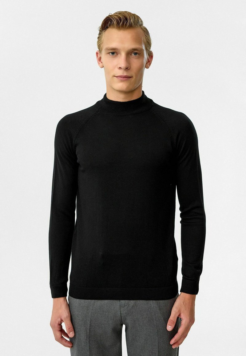 Zwarte coltrui met lange mouwen, gemaakt van een fijn gebreid materiaal. Heeft een aangesloten ontwerp en ribgebreide manchetten en zoom.