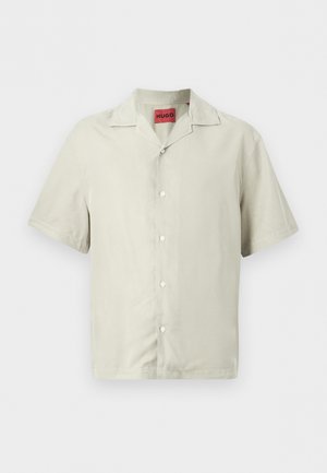 Chemise beige à manches courtes avec boutons, col camp et étiquette rouge HUGO à l'intérieur du col, présentée sur un fond uni.