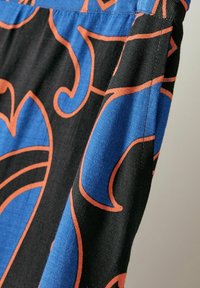 Svart tyg med stora blå och orange virvlande mönster; har en slät textur och elastisk midja. Närbild som framhäver sömnadsdetaljer.