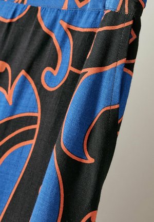 Tessuto nero con grandi motivi blu e arancioni a spirale; presenta una superficie liscia e una vita elasticizzata. Vista ravvicinata che mette in risalto i dettagli dei punti.