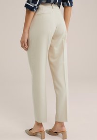 Pantalons ajustés couleur crème avec une taille haute, des poches latérales et une texture lisse. Associés à des chaussures à talons blocs beiges.