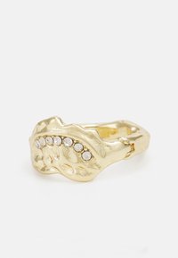Bague dorée avec un design texturé et ondulé, comportant une rangée de six petites pierres claires en haut. Forme minimaliste et audacieuse.