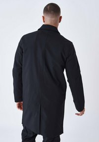 Langer schwarzer Mantel mit maßgeschneiderter Gestaltung und glatter Textur, ausgestattet mit einem Rückenschlitz und detaillierten Nähten. Geeignet für einen formellen Look.
