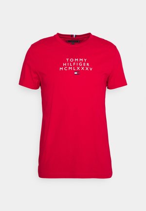 Czerwona bawełniana koszulka z białym napisem "TOMMY HILFIGER MCMLXXXV" i małym wzorem flagi umieszczonym centralnie pod napisem. Krótkie rękawy, okrągły dekolt.