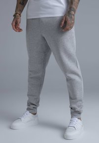 Gray sweatpants made of soft fabric, featuring a tapered design, elastic cuffs, and side pockets, paired with white sneakers.