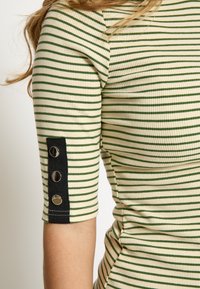 Top de rayas con colores verde y crema, textura acanalada y mangas cortas con acentos de tela negra y tres botones metálicos.