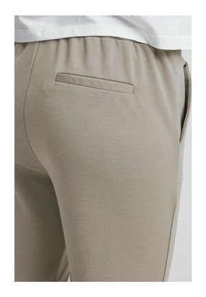 Beige jogger pants with a smooth texture, elastic waistband, and a single back pocket, detailed stitching along the seams.