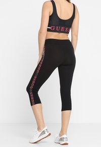 Leggings sportivi neri di lunghezza al polpaccio, con un motivo a catena rosa sul lato e un reggiseno sportivo a rete nera cropped.