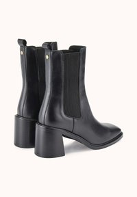 Bottines noires en cuir avec des panneaux élastiques côtelés et un talon bloc cylindrique. Texture lisse avec des tirants fonctionnels à l'arrière.