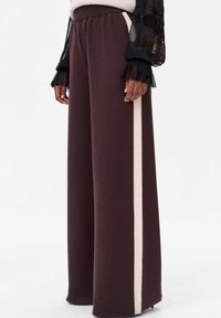 Wijde bordeauxrode broek van zachte stof, met een beige zijkantstreep. Elastische tailleband en een losse pasvorm voor comfort.