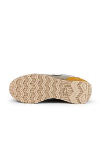 Suela de zapatilla con un patrón de agarre en zigzag, con acentos en gris, negro y amarillo. Fabricada con materiales de goma y textil, diseñada para ofrecer tracción.